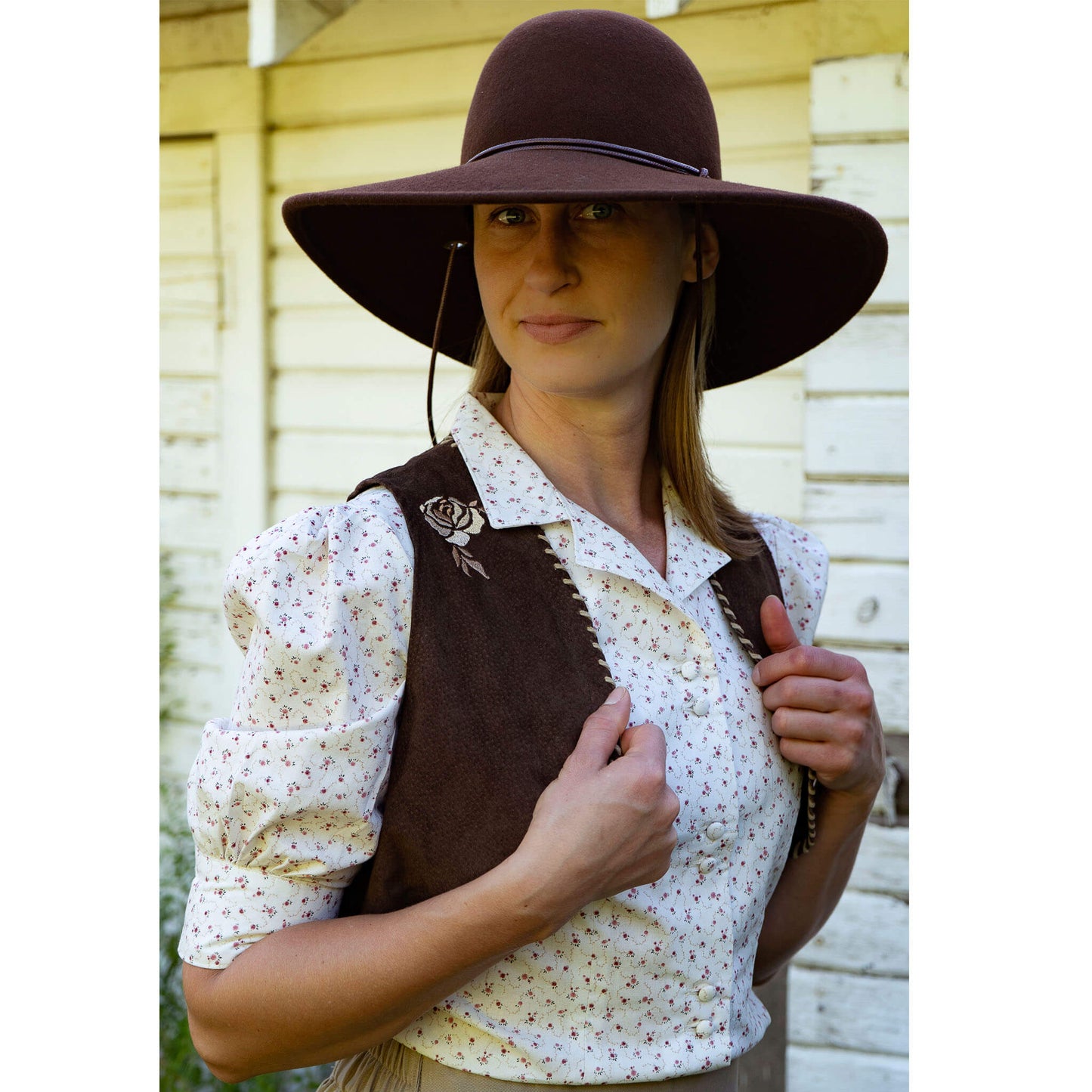 With our admiration for Prairie Rose Henderson came the Prairie Rose Vest. Champion bronc rider Rose is not only known for her daring feats in the arena but also dazzled the crowds with her beautiful and inventive performance costumes. Made of  brown pigskin suede with a signature embroidered rose. Edges are whip-stitched in a beige leather lace. Lined in Polyester. Made in USA.