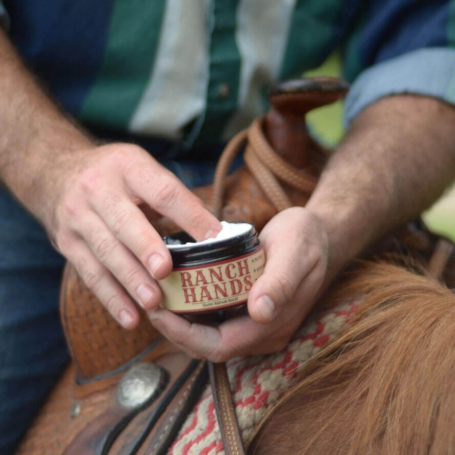 Person holding a jar of 'Ranch Hands' product on a horse saddle