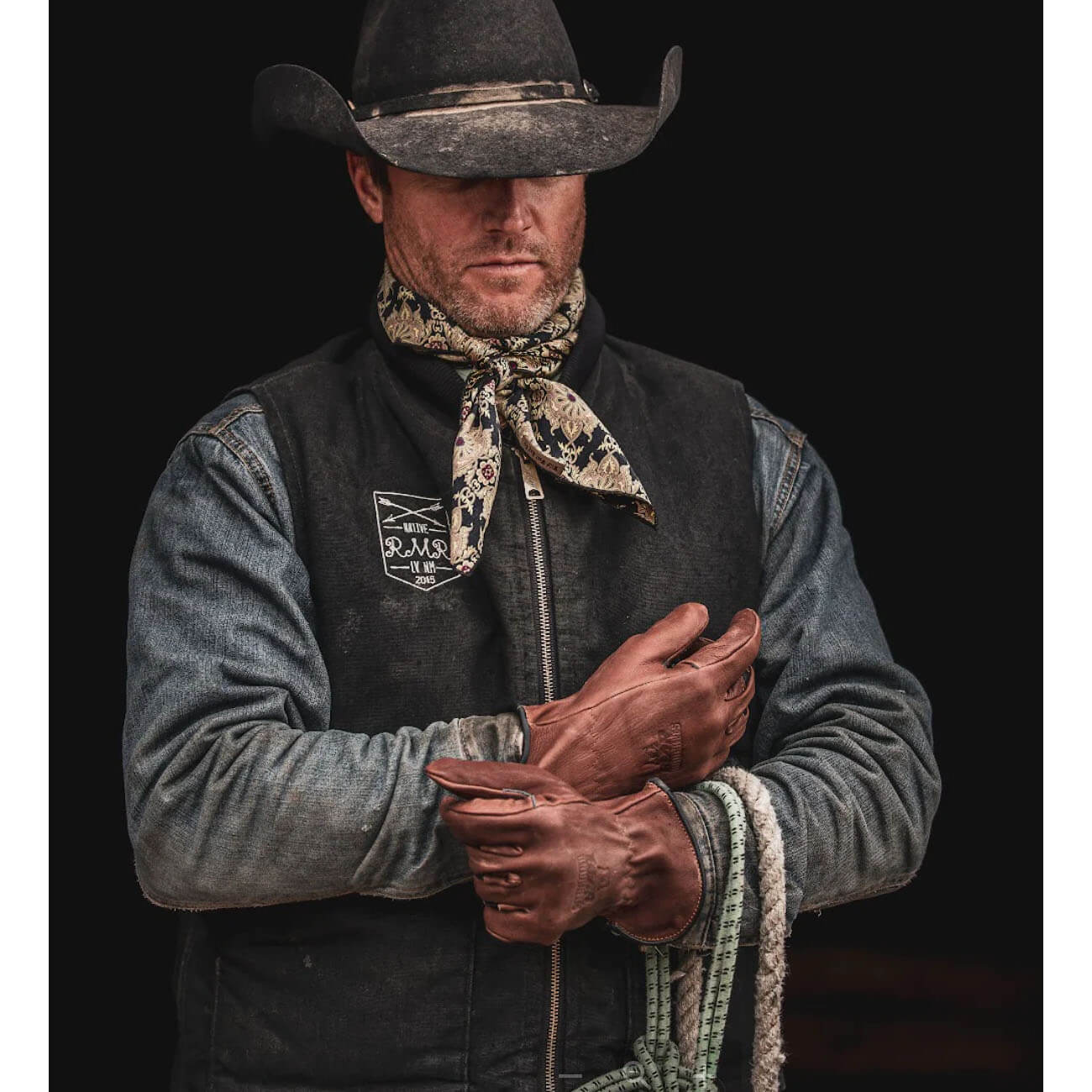 Man wearing a cowboy hat and rugged clothing with a dark background