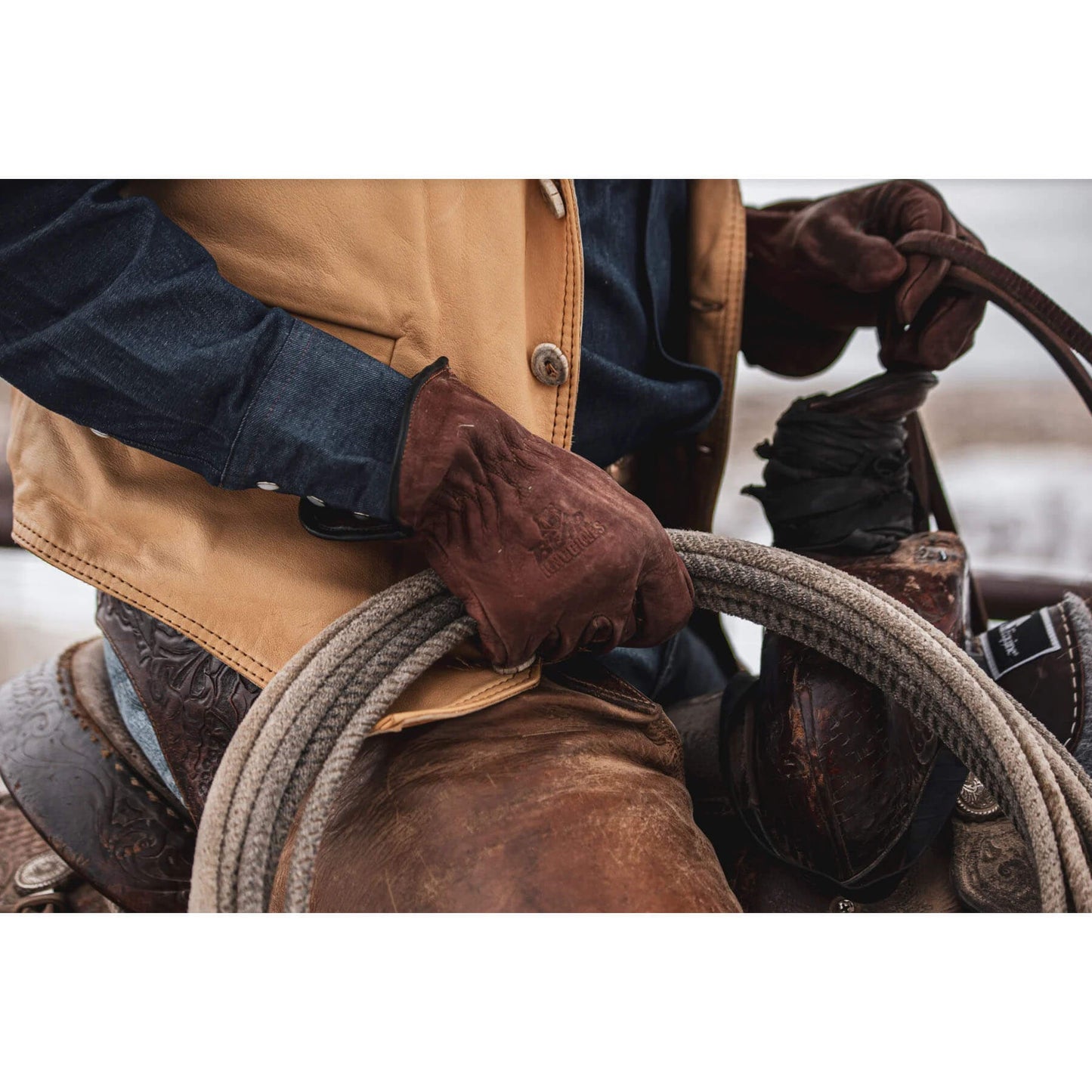 Person wearing a brown leather jacket and gloves holding a rope, with a blurred background