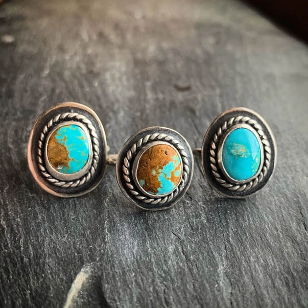 This sterling silver ring features a piece of American Turquoise, known for its color ranges of blues, greens, browns and blacks. Each silver design element of each ring is made by hand and soldered together. The Turquoise for these rings will vary in color, pattern, shape and sometimes slightly in size. Material: Sterling silver, American Turquoise. Size: Each ring measures approximately .75" in length, but may vary depending on stone shape.