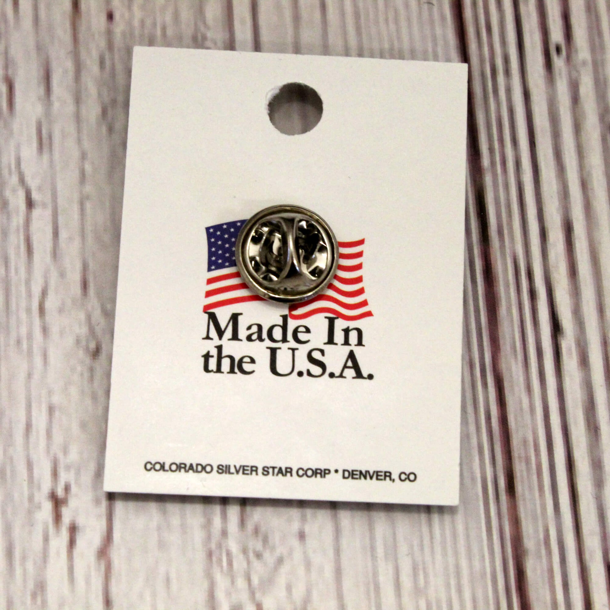 Pin with American flag design on a 'Made in the U.S.A.' card, on a wooden surface.