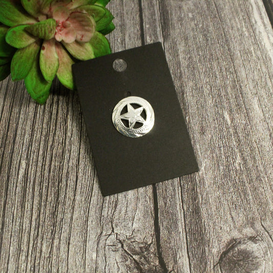 Silver star-shaped pin on a black card with a green plant in the corner on a wooden surface