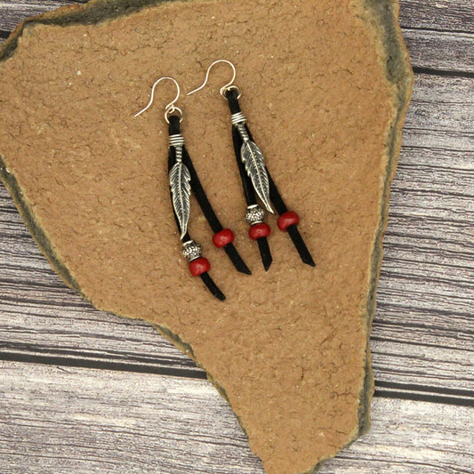Pair of feather-themed earrings with red beads on a stone surface