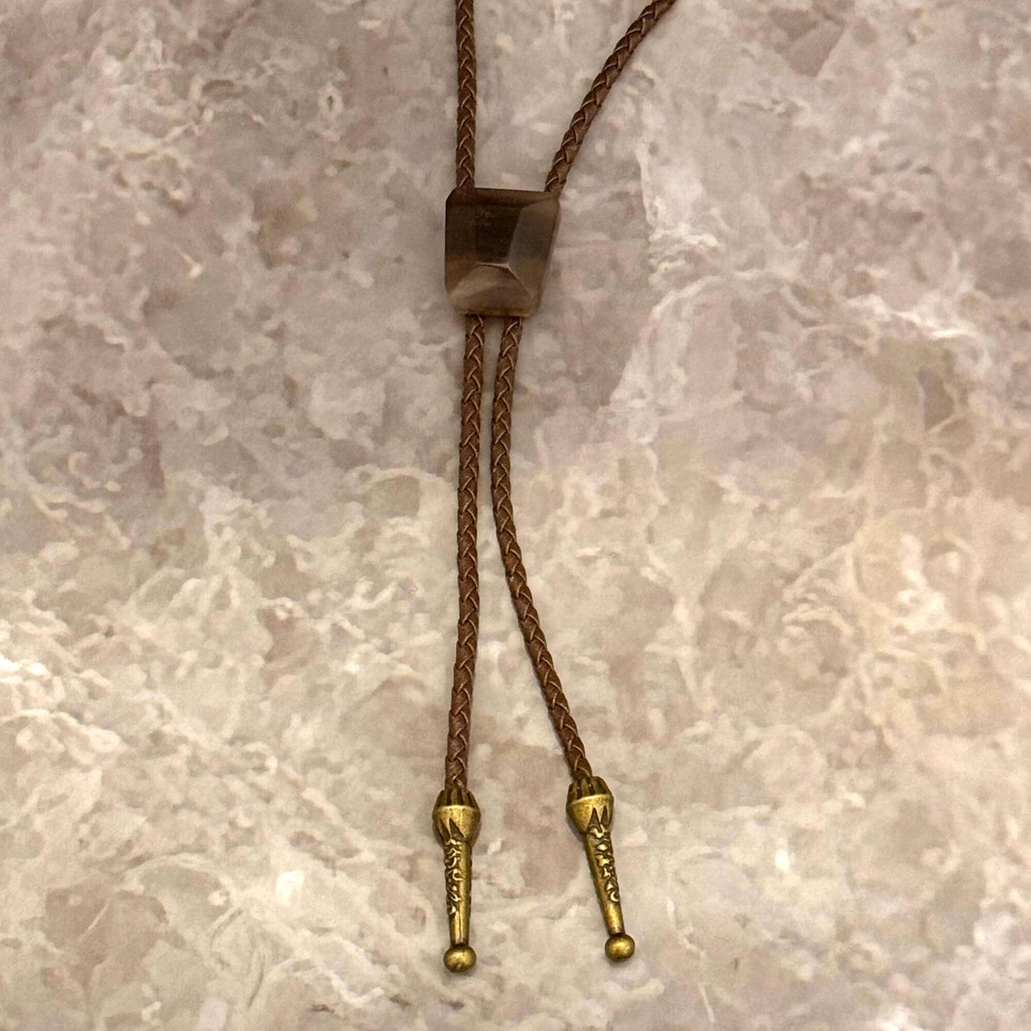 Brown braided cord with gold metal ends on a marble surface