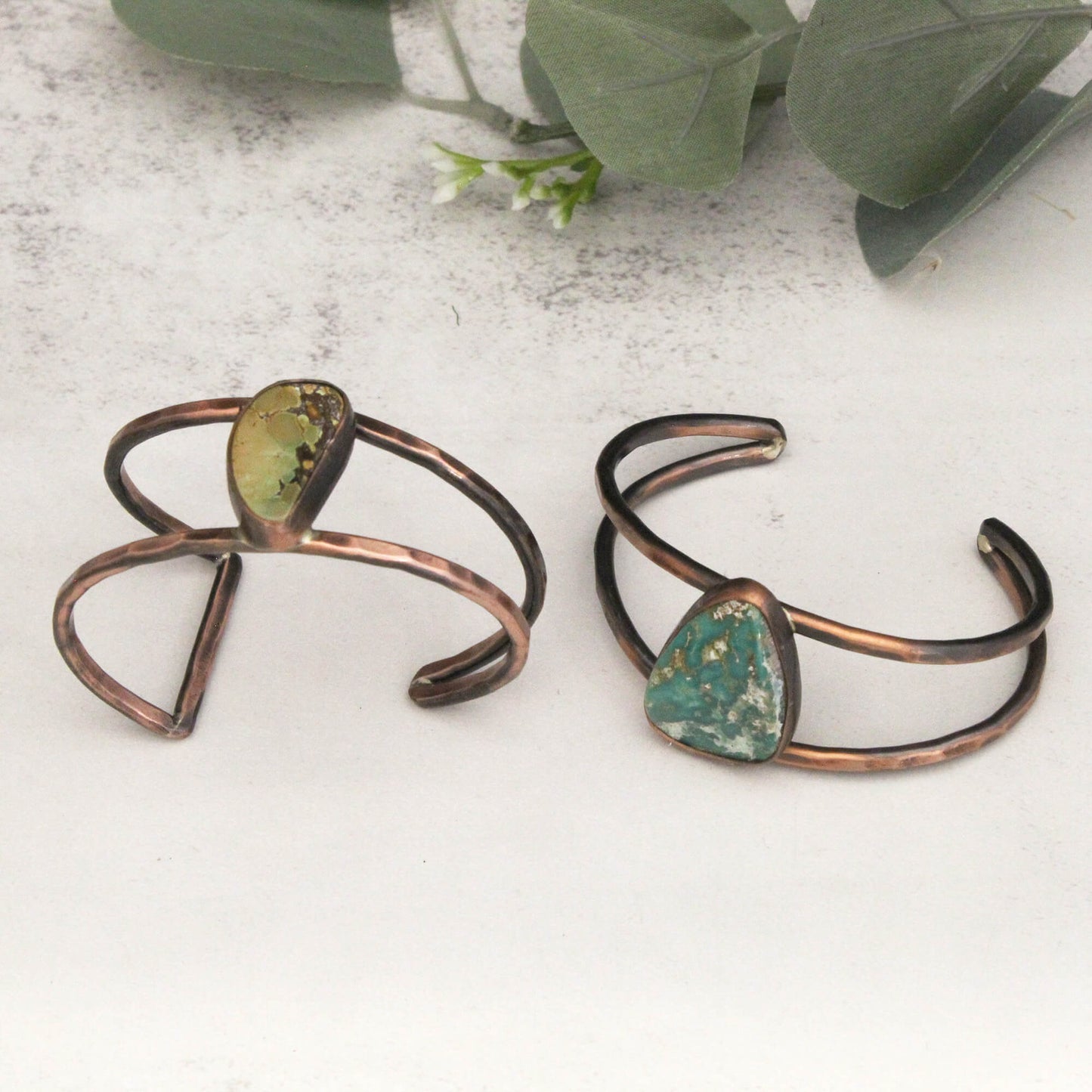 Two copper bracelets with green stone accents on a light surface.
