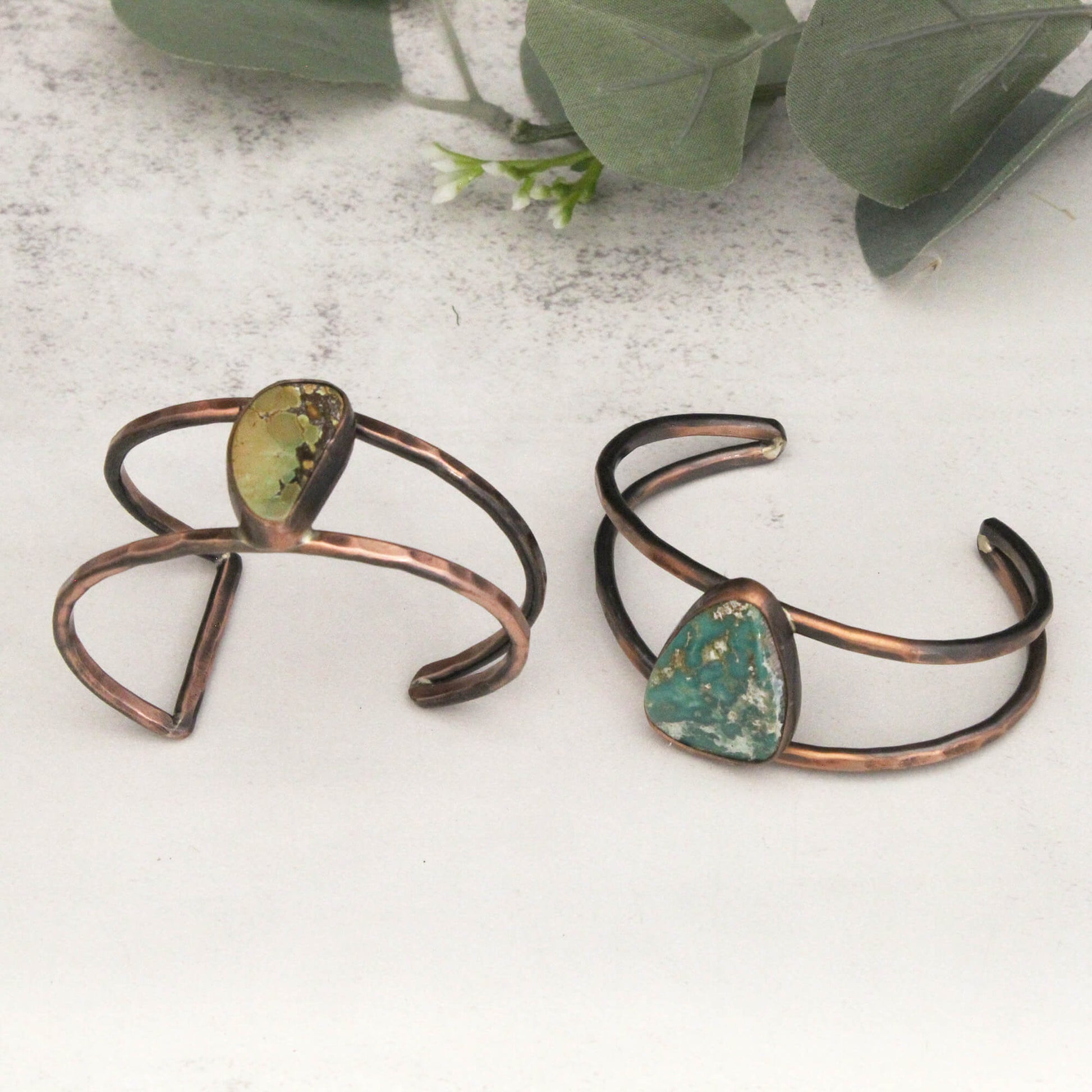 Two copper bracelets with green stone accents on a light surface.