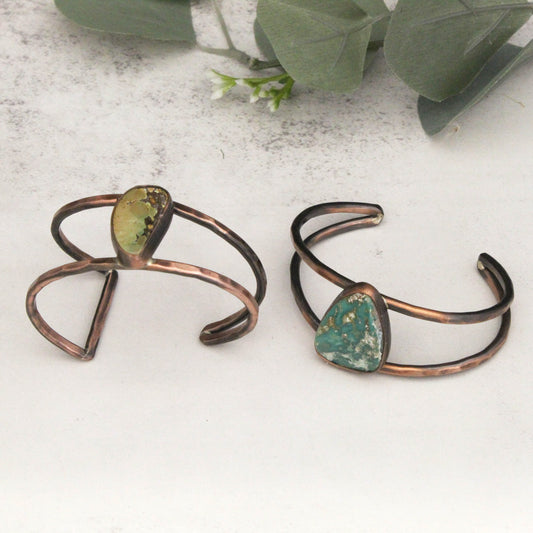 Two copper bracelets with green stone accents on a light surface.