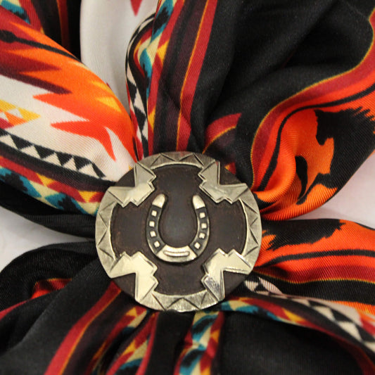 This southwestern style scarf slide features a distinctive horseshoe design, elegantly complemented on a round black metal Concho. The Concho not only enhances the aesthetic appeal but also provides functionality, with loops on the back that securely attach it to your scarf. Ideal for adding a touch of cultural flair to any outfit, this scarf is a perfect accessory for those who appreciate unique craftsmanship and heritage. Measures 1-1/2" Diameter