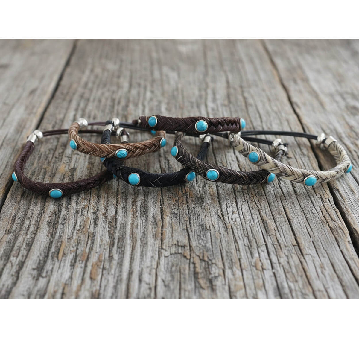 Four braided horsehair bracelets with turquoise stone accents and silver-toned metal beads, arranged on a rustic weathered wood surface.