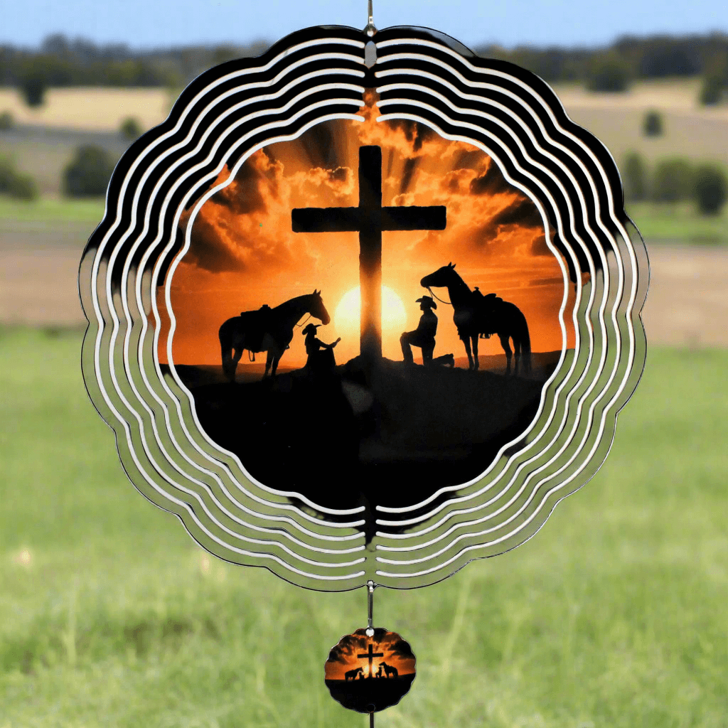 Decorative wind chime with silhouette of horses and cross against sunset, set against a grassy field.