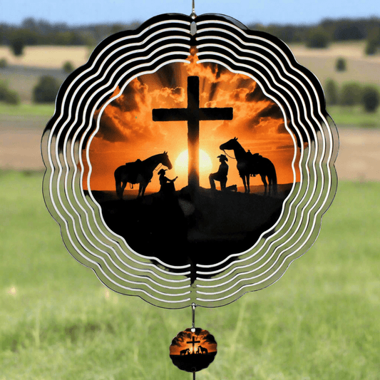 Decorative wind chime with silhouette of horses and cross against sunset, set against a grassy field.