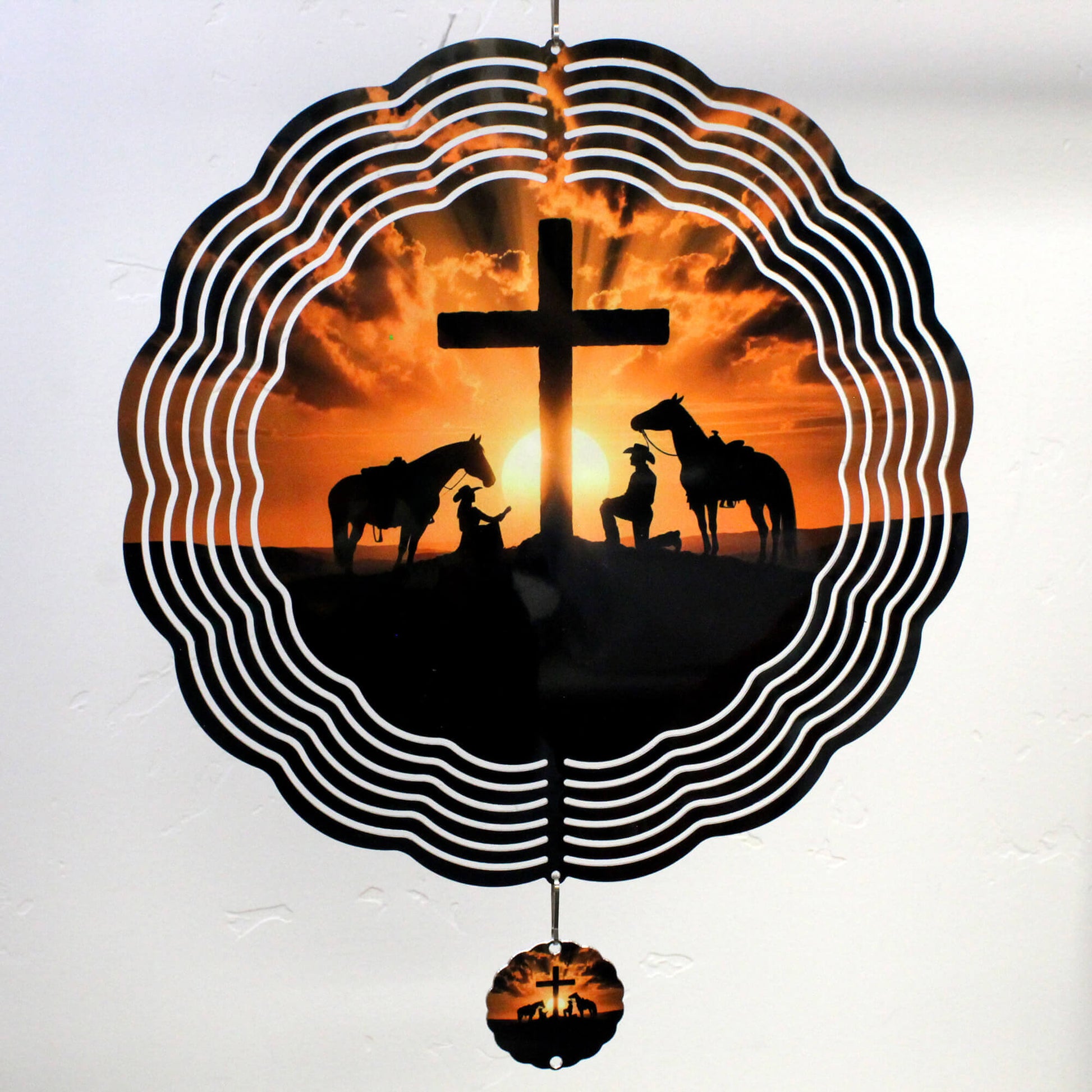 Decorative wall hanging with silhouette of a cross, horses, and people against an orange sunset sky.