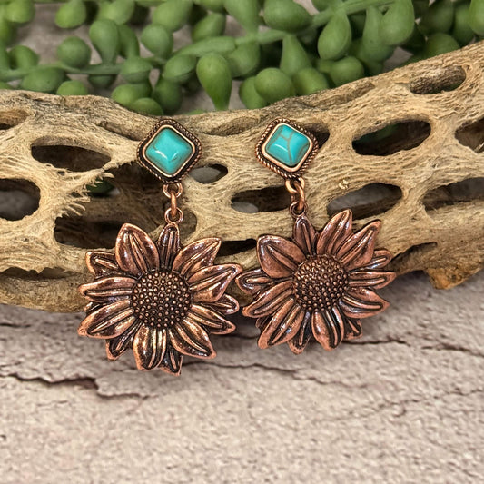 Copper sunflower earrings with turquoise stones on a natural wood and green plant background
