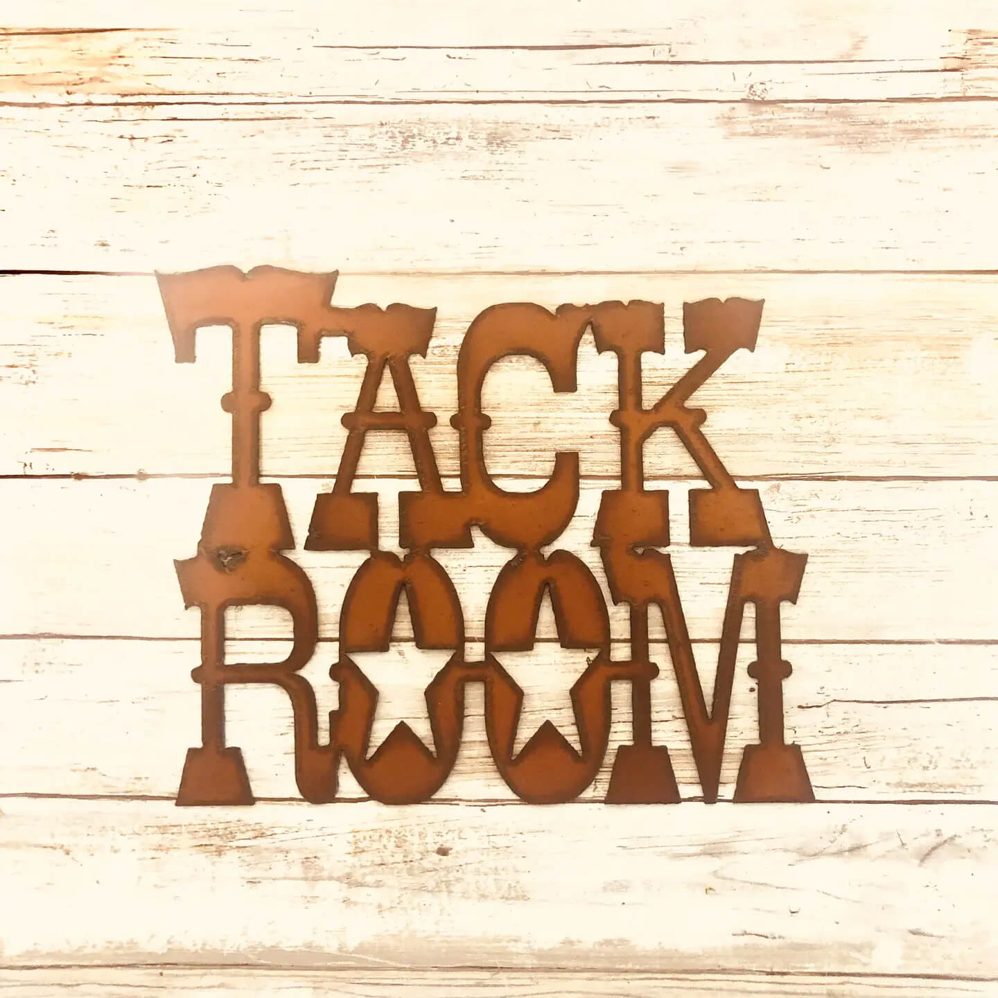Copper-colored metal wall art spelling 'TACK ROOM' in a rustic western-style font, displayed on a light wood plank background.