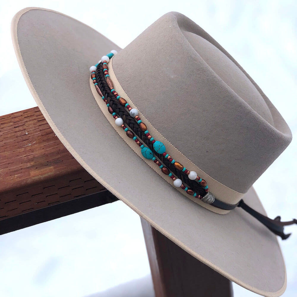 On trend, the Taos Hatband features a seven strand braid of Authentic Horse Hair complimented by two strands of coppery metal beads, white and turquoise howlite, and freshwater pearls. Finished with our sunburst Conchos, leather tassels and secured with a horse hair knot.  One size fits most hats. Hat not included. Made in USA