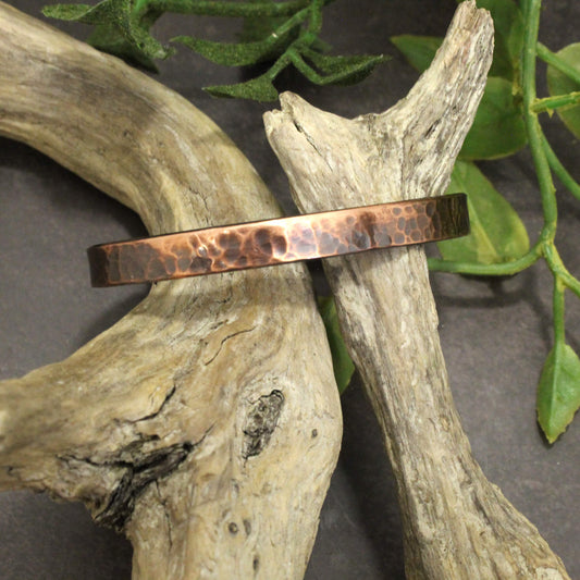 Copper bracelet on a piece of driftwood with green leaves in the background