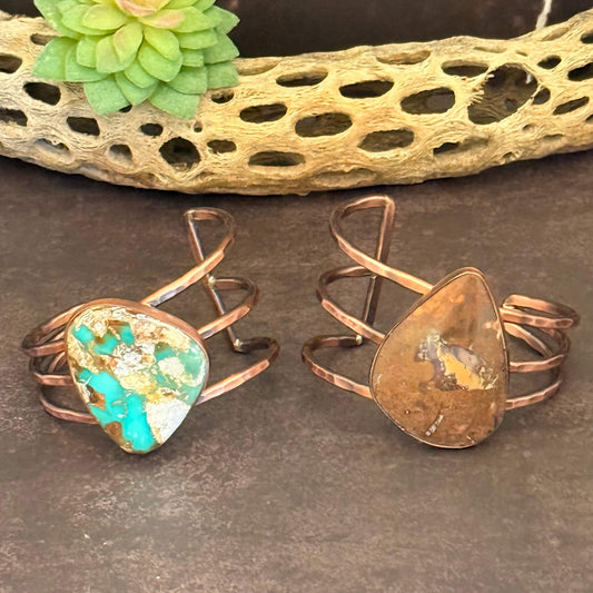 Two copper rings with stone inlays on a textured surface.