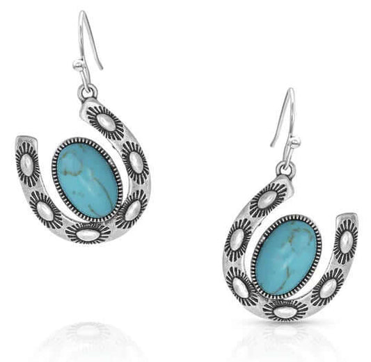 The image features a pair of Western ladies' silver horseshoe earrings that showcase a turquoise stone set within an antique silver finish over a brass base. These earrings are designed with hypoallergenic stainless steel French hooks, making them both stylish and comfortable to wear. They serve as a fashionable accessory and highlight the beauty of gemstone jewelry.