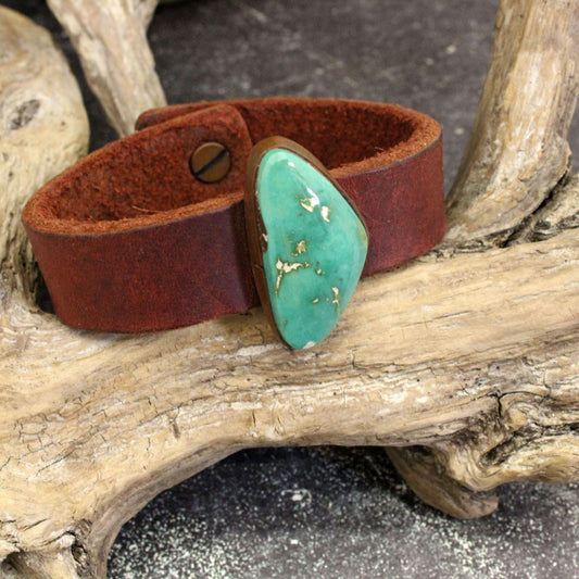 Brown leather bracelet with a turquoise stone on a wooden branch