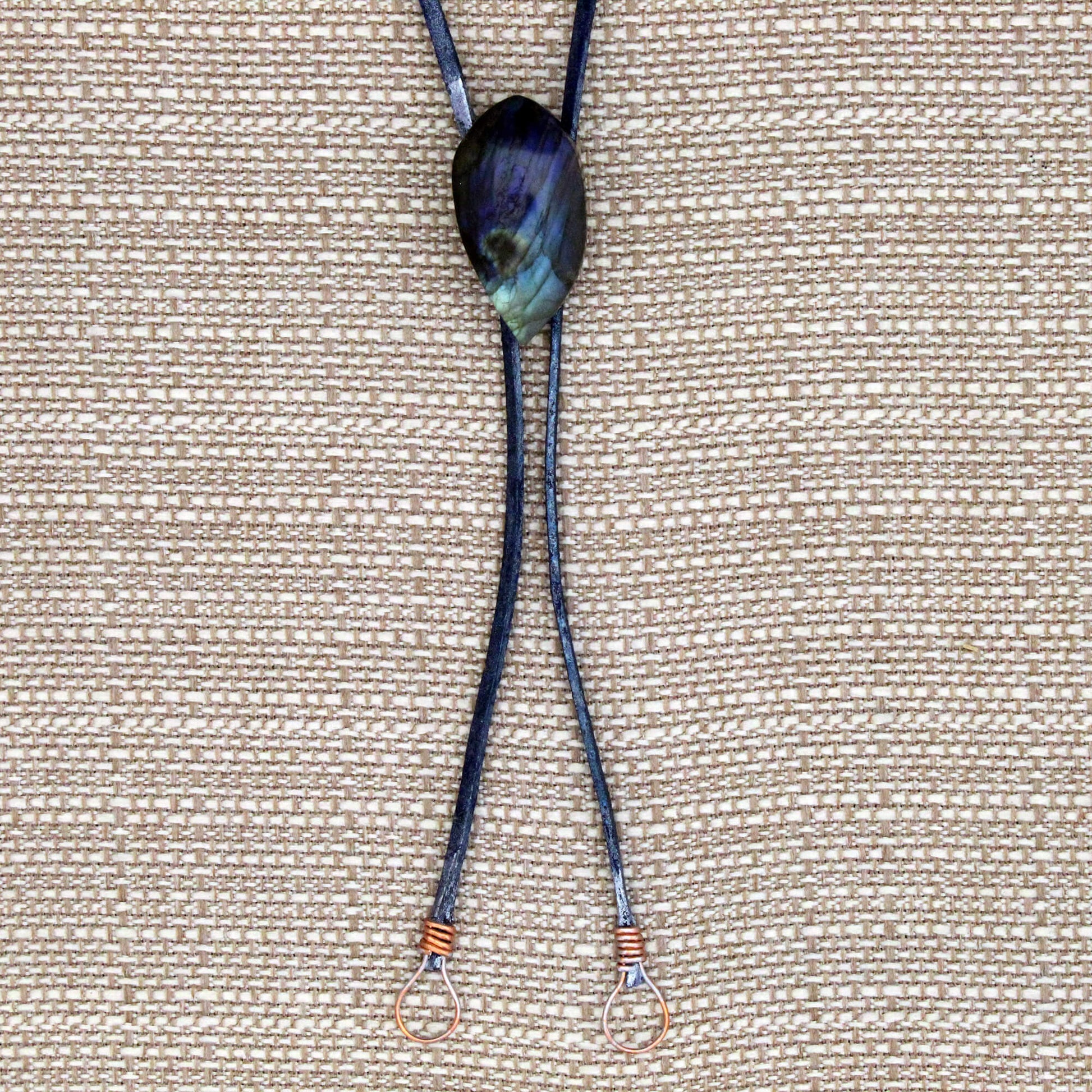 Necklace with a dark blue cord and a large, multicolored stone pendant on a beige fabric background.