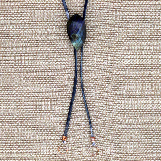 Necklace with a dark blue cord and a large, multicolored stone pendant on a beige fabric background.