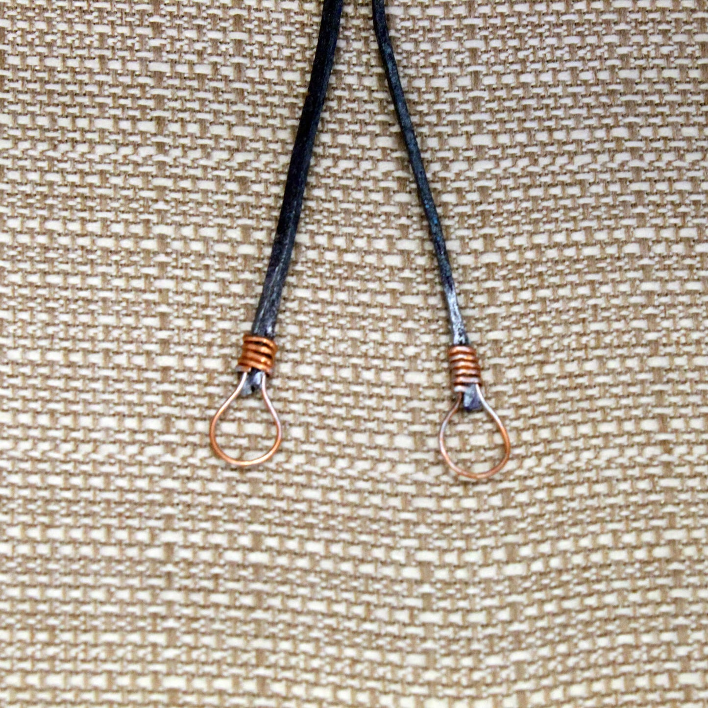Two bolo tie ends on a textured beige background