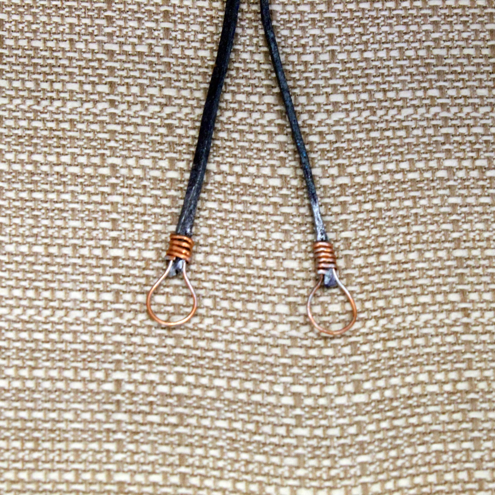 Two bolo tie ends on a textured beige background