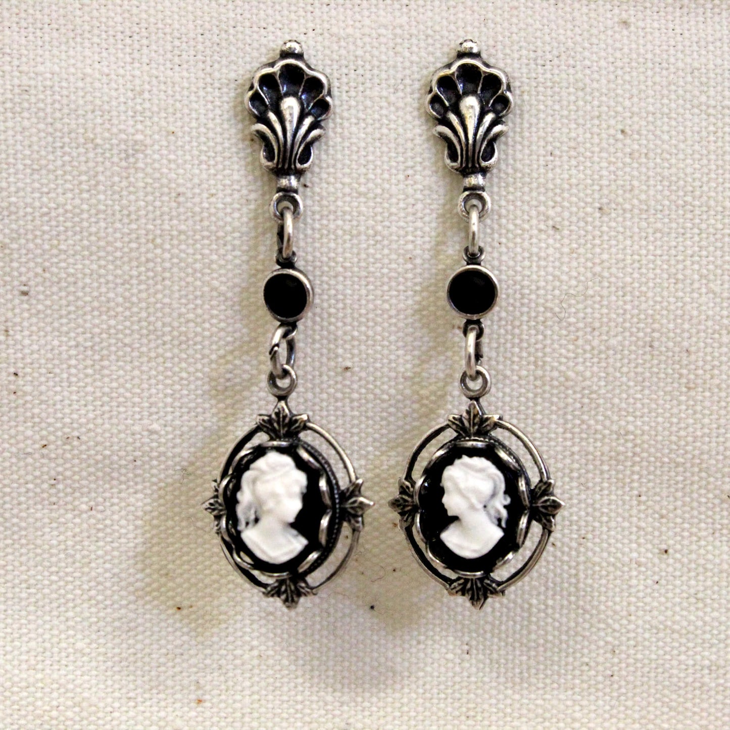 Pair of silver earrings with black stones on a beige fabric background