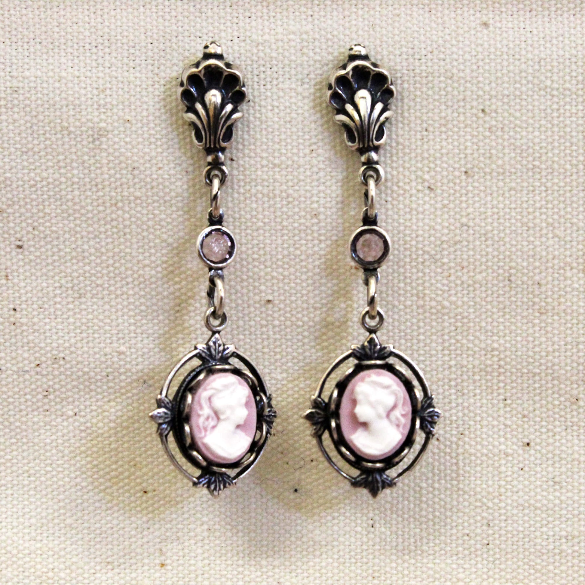 Pair of silver earrings with pink cameo stones on a beige fabric background