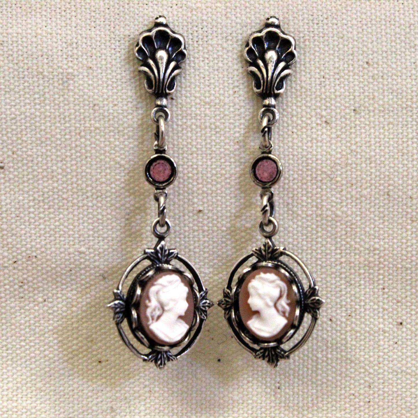 Pair of silver earrings with cameo designs on a beige fabric background