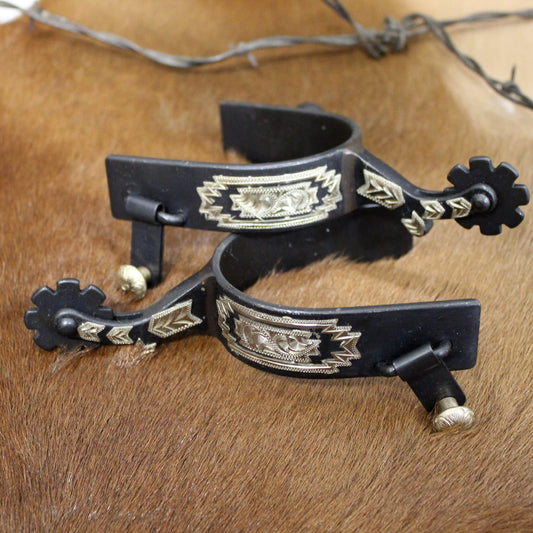 These antiqued spurs feature a 2" shank, a 1" band and an 8 point rowel. Engraved German silver trim adds the perfect detail to these spurs. Antique brown spurs with engraved silver southwest design overlay.