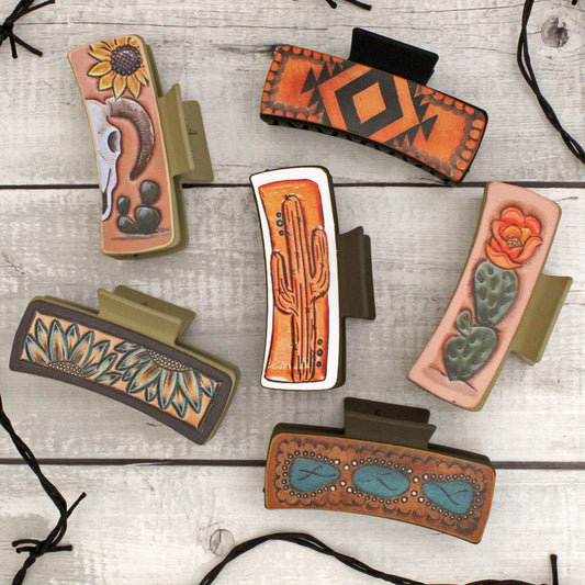 Collection of decorative hair clips with tribal and nature-themed designs on a wooden surface.
