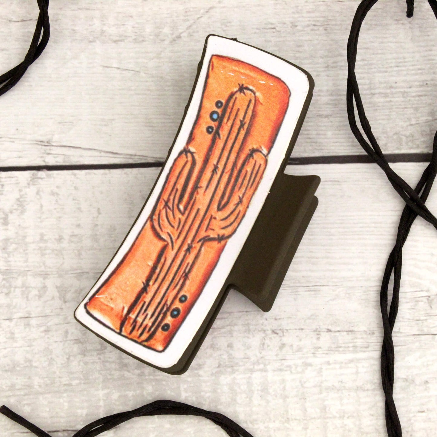 Hair claw with a cactus design on an orange background, placed on a light wooden surface.