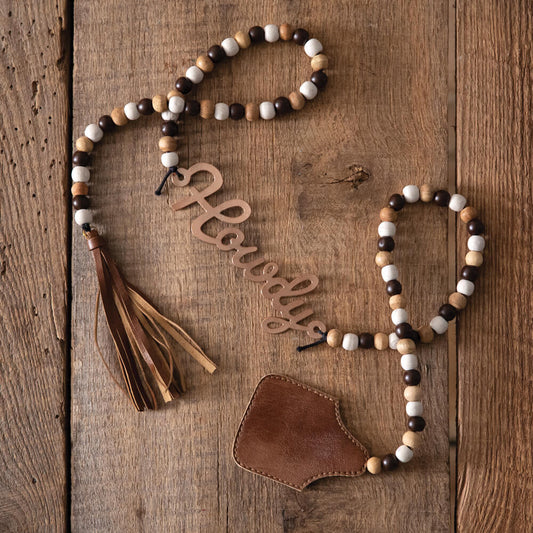 Howdy! Use these beads to add texture and western charm to your two-tier trays, walls, or any way you can imagine! Each strand has wood beads surrounding an antique copper metal ''howdy'' and a leather tassel and ear tag on the ends. Measurement: 49''W x 3''H