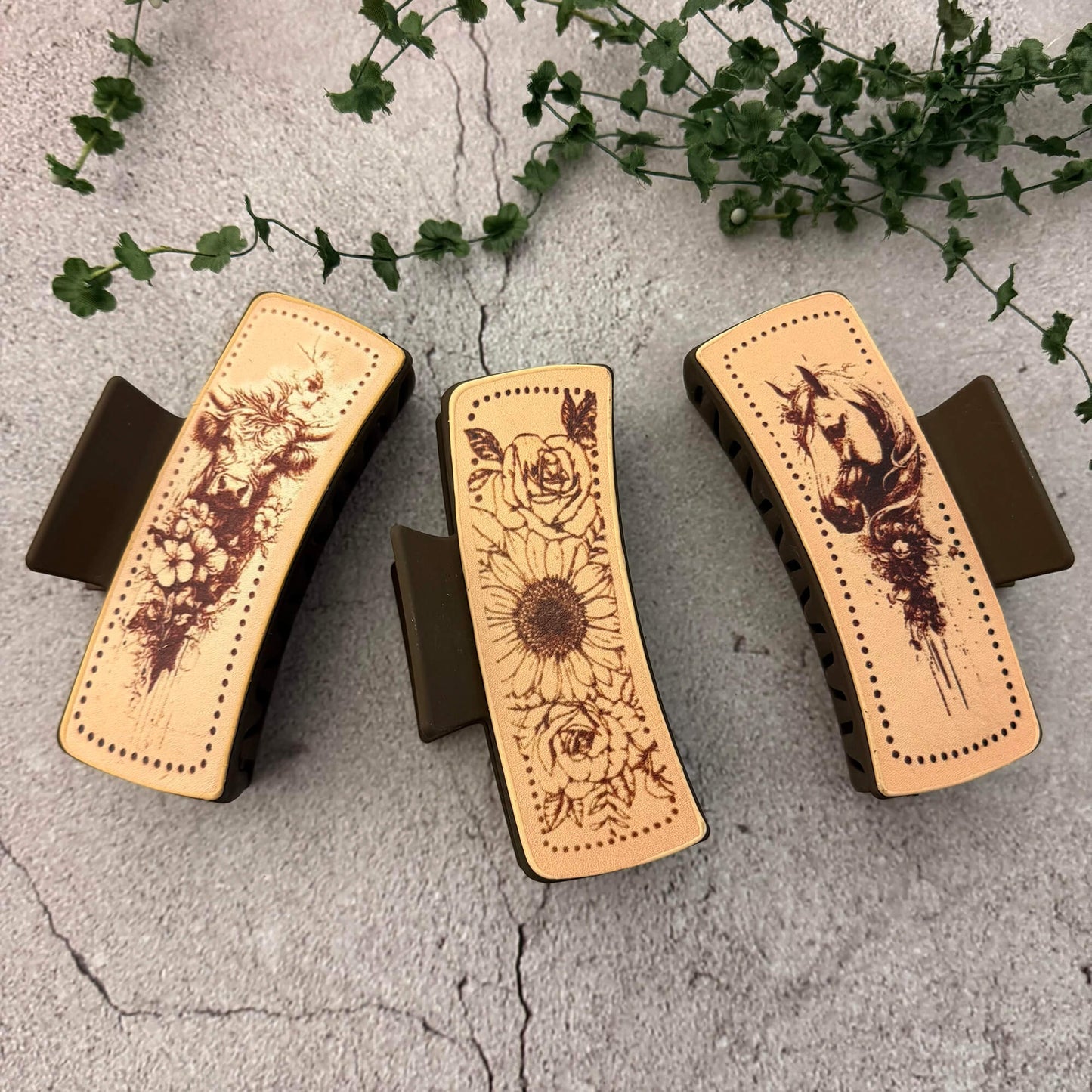 Three hair clips with designs on a textured surface with greenery.