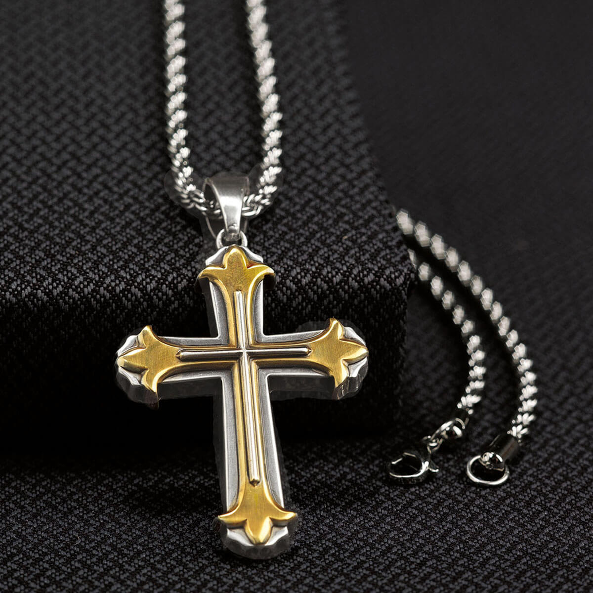 Two-tone cross pendant necklace on a black textured background
