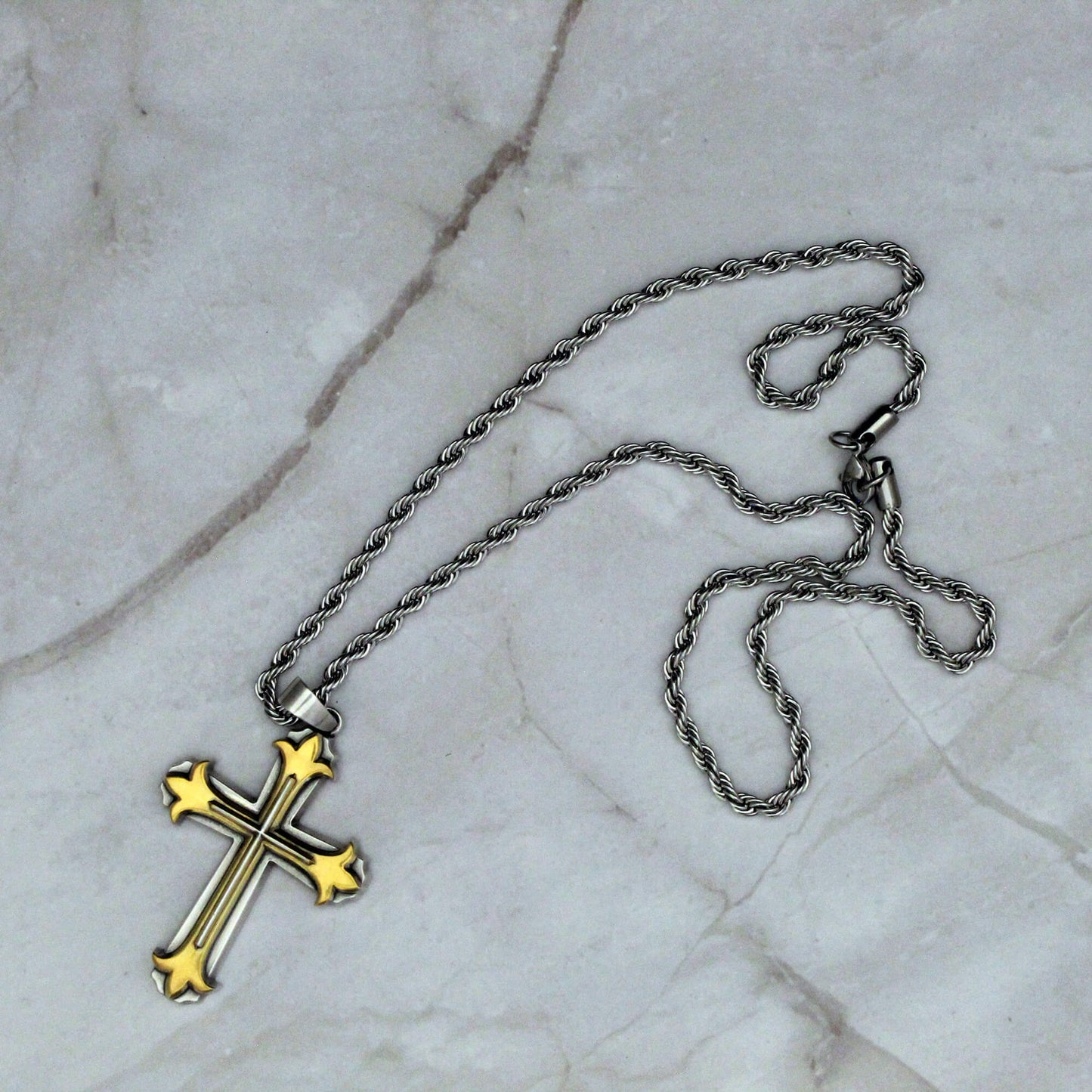 Gold cross pendant on a silver chain against a marble background