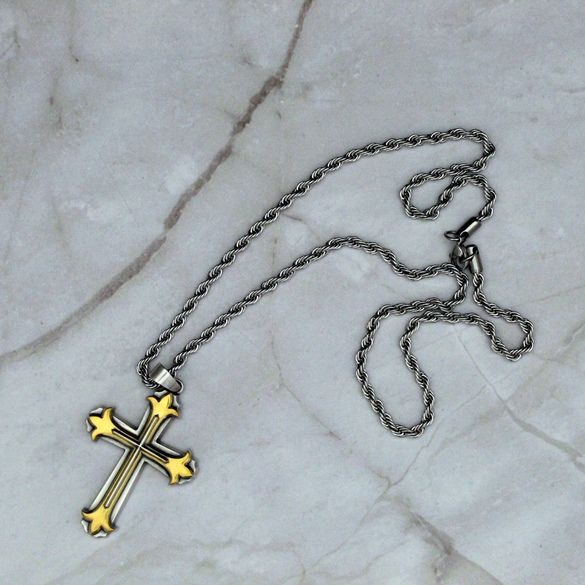Gold cross pendant on a silver chain against a marble background