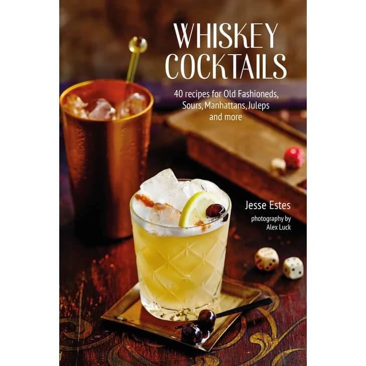Book cover for 'Whiskey Cocktails' by Jesse Estes, featuring a whiskey glass with a yellow cocktail, ice, a lime wheel, and cherries on a dark wooden table, alongside a copper-colored tumbler in the background.