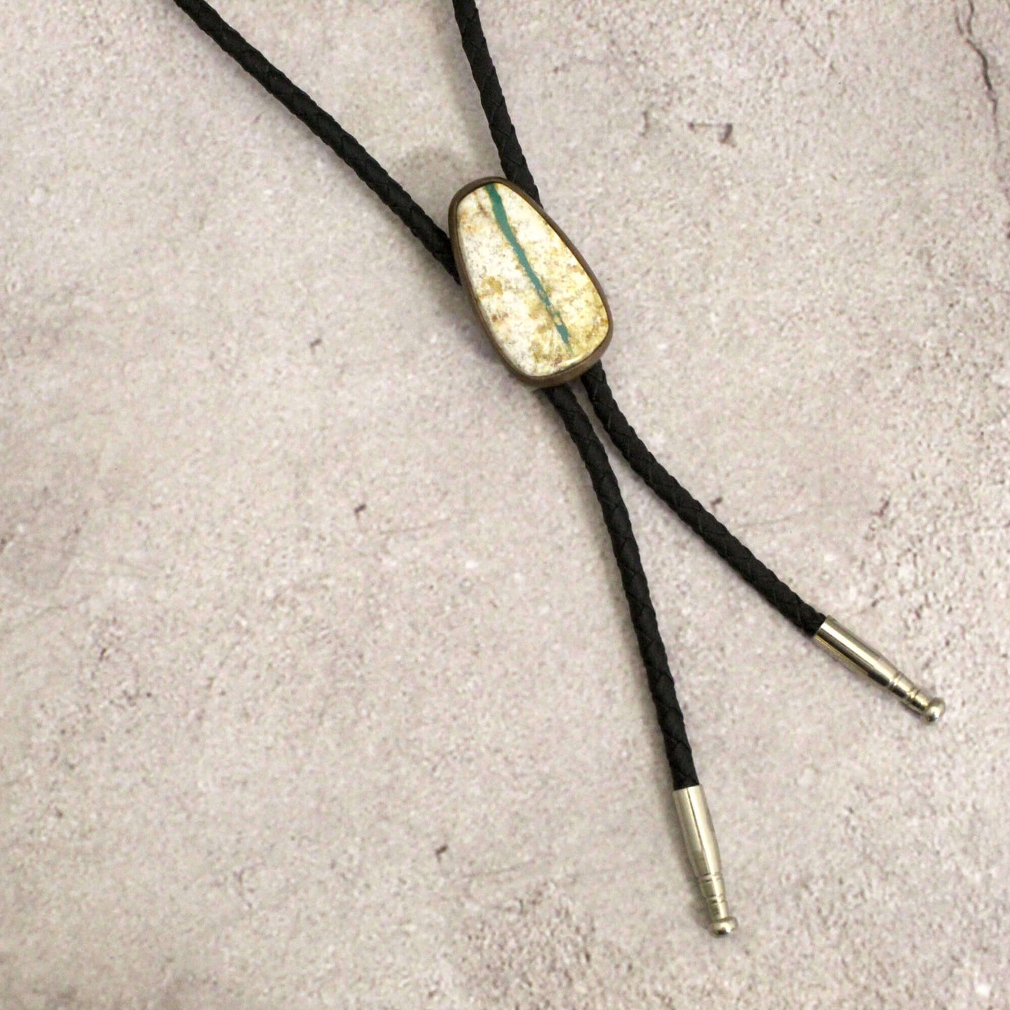 Bolo tie with gold and green stone on a concrete surface