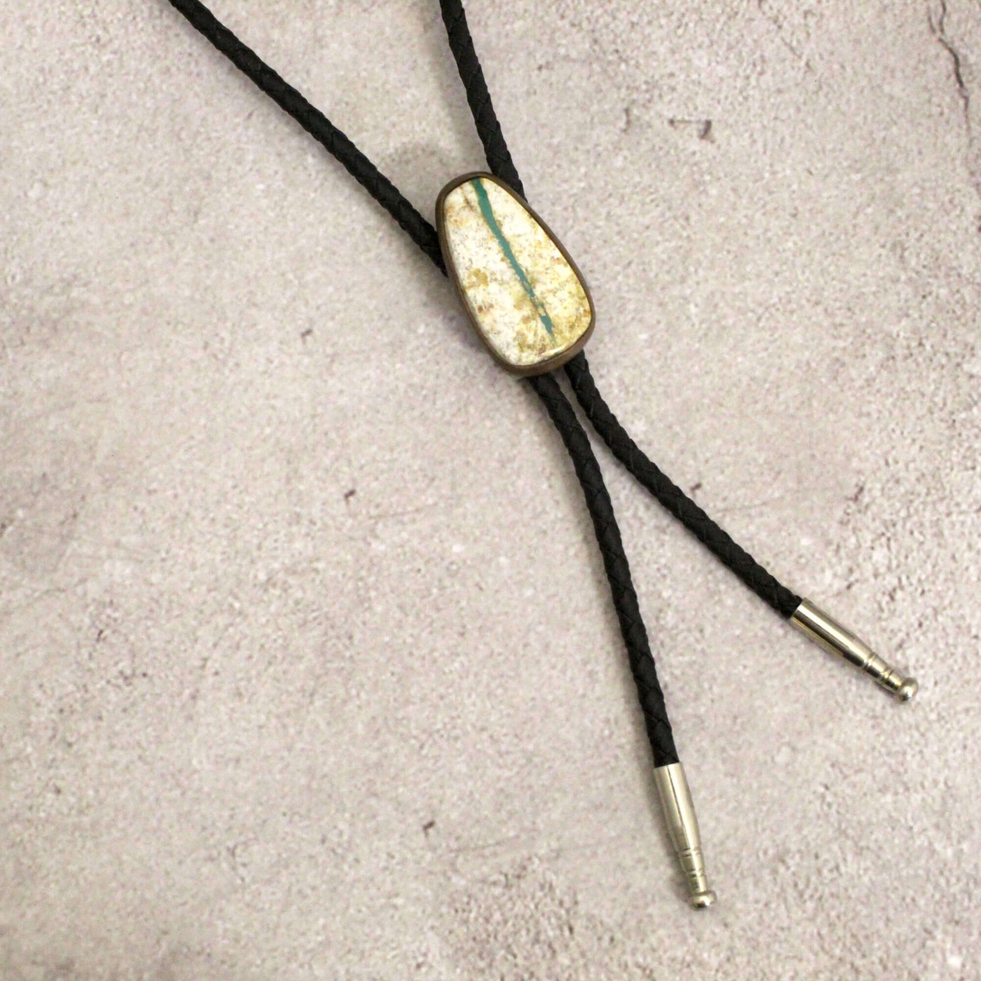 Bolo tie with gold and green stone on a concrete surface