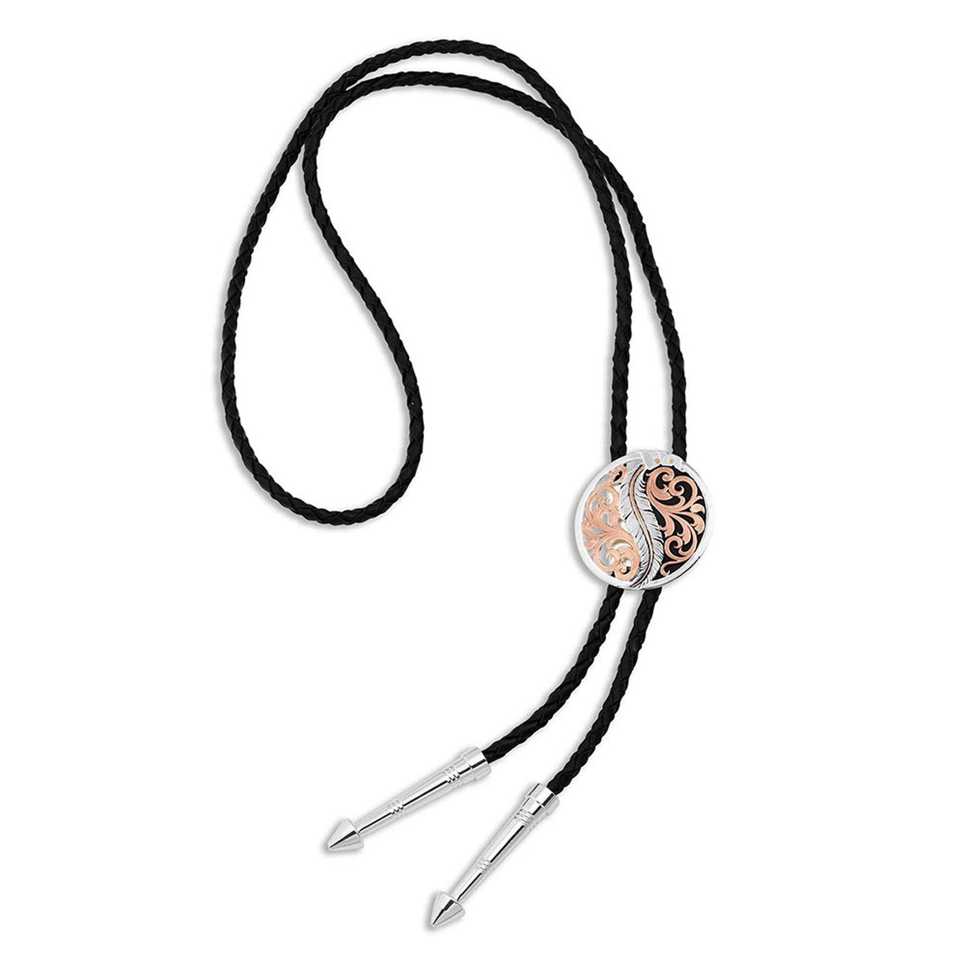 A small portrayal of silver artistry combining 18 karat rose gold and fine silver finishing on this pierced bolo tie. A round concho with a center antiqued silver finished feather bending as if it is being pushed by the wind is bracketed by rose gold filigree scrollwork. The detailed feather has a thin center rose gold finished vein accenting the light antiquing of the feather.