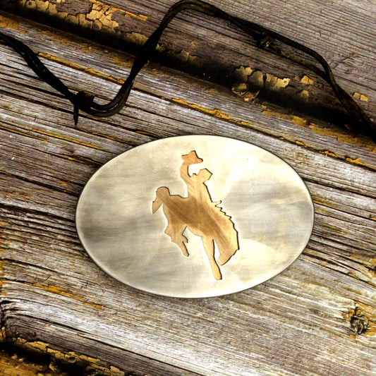 Gold belt buckle with cowboy silhouette on a wooden surface