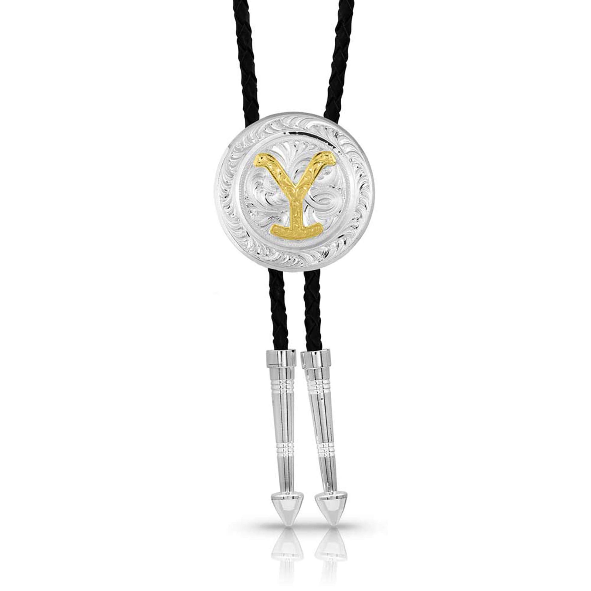 A licensed Paramount TV series Yellowstone concho bolo tie. This bright silver-finished round concho has classic bright-cut engraving flowing throughout the piece with an antiqued gold-finished figure of the Yellowstone, Dutton family brand Y in the center circle. Braided leather cords have silver toned tips.