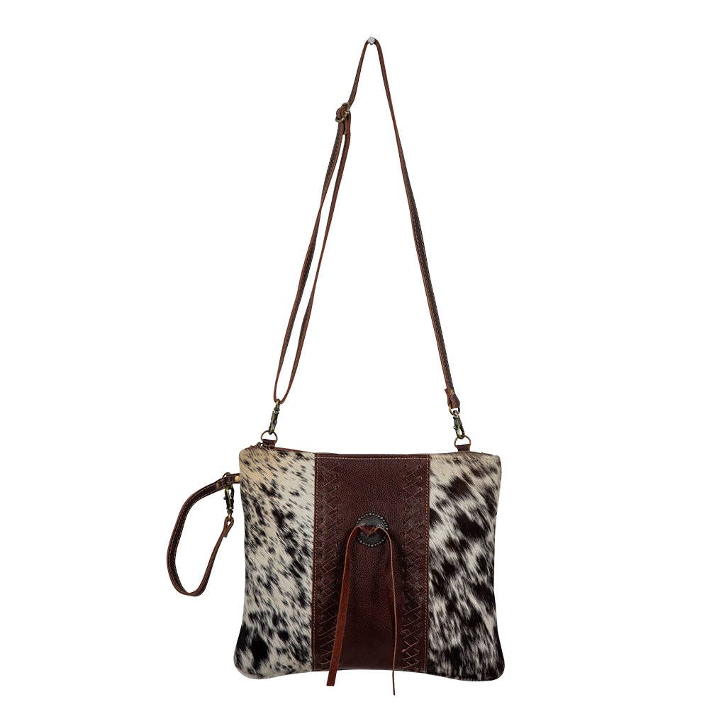Crossbody bag with cowhide pattern and brown accents on a white background