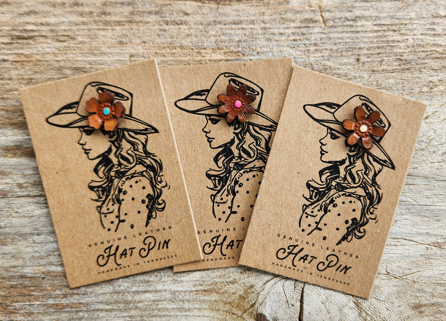 Three hat pins with decorative flowers on brown paper packaging against a wooden background