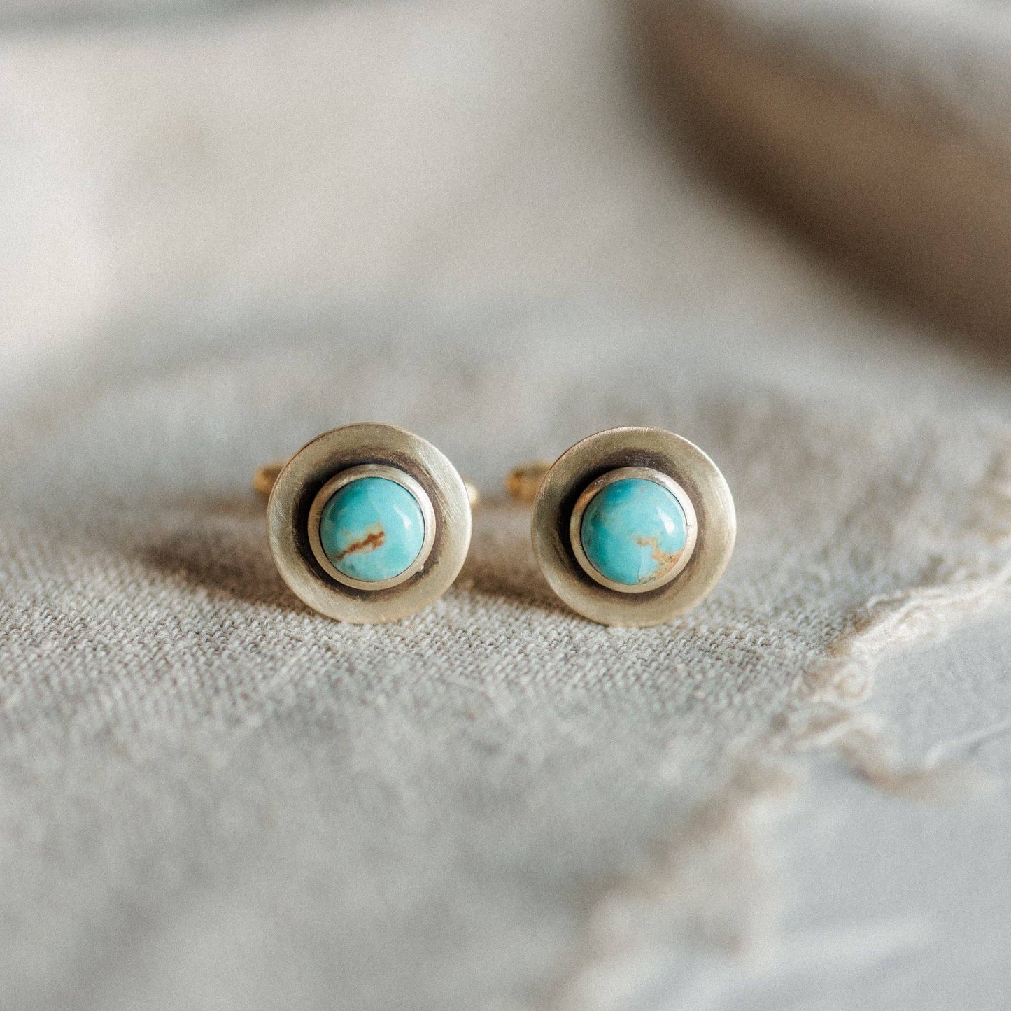 Pair of gold earrings with turquoise stones on a textured beige surface