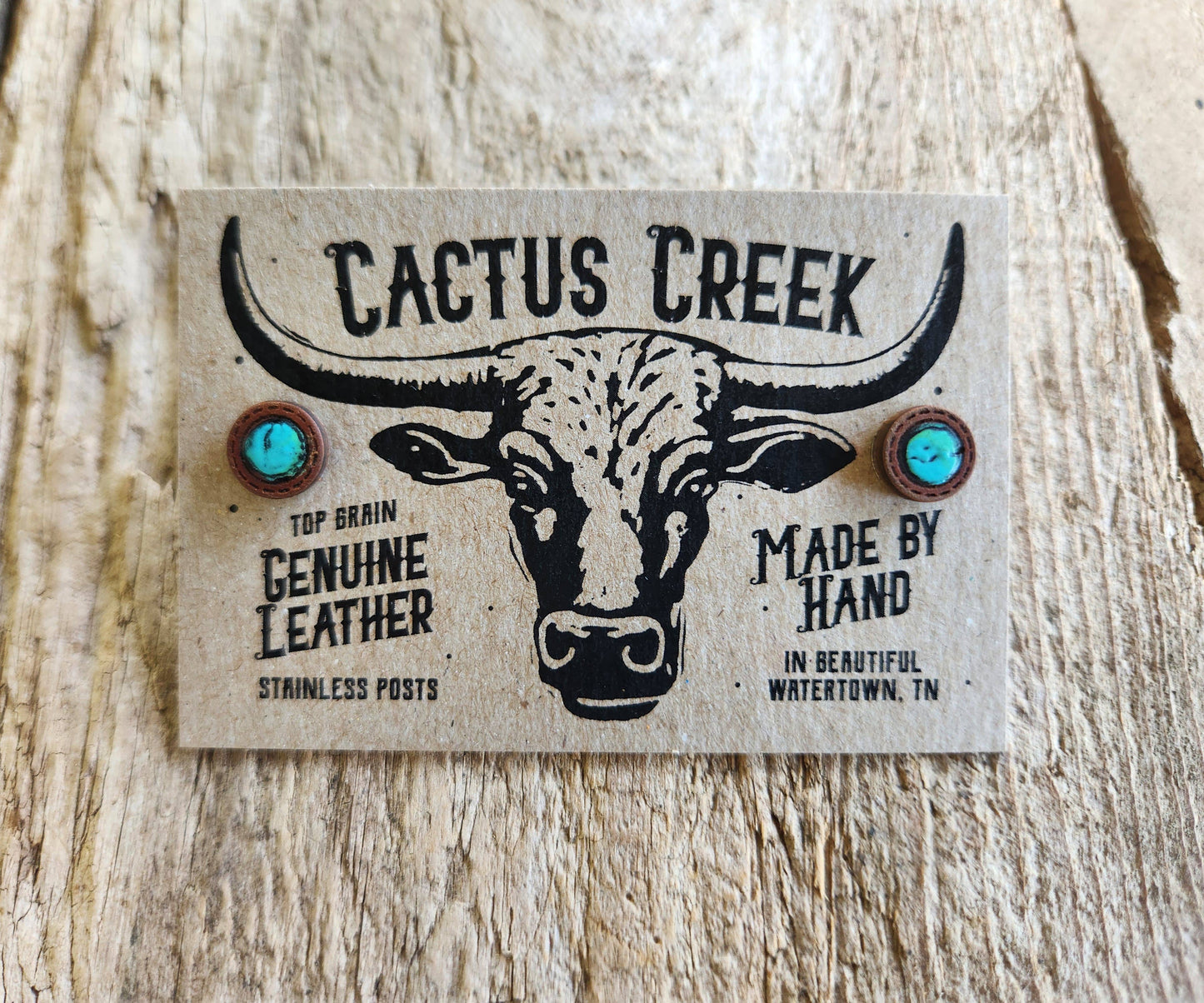 Pair of earrings with 'Cactus Creek' branding on a wooden background