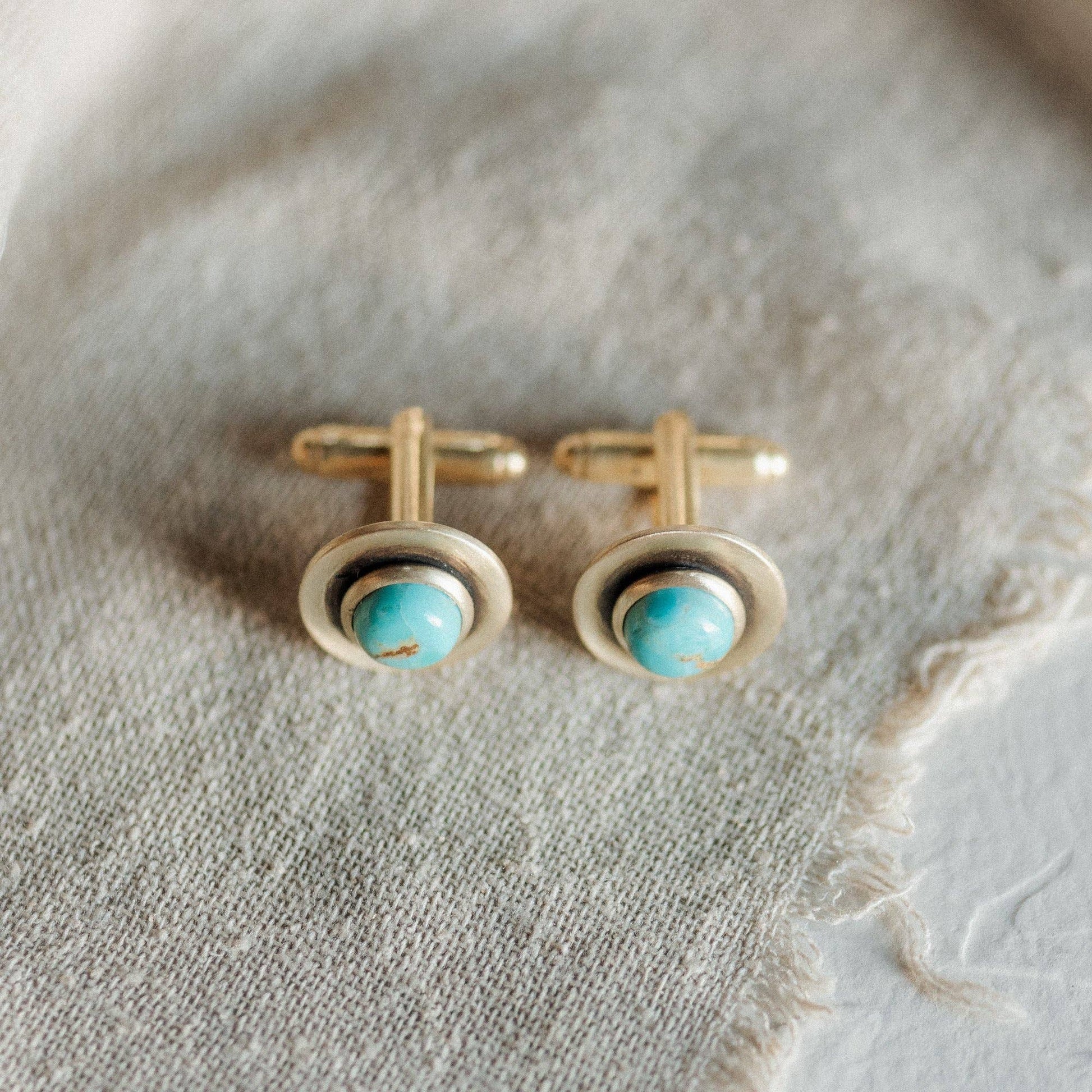 Gold cufflinks with turquoise stones on a textured fabric background